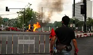 En enlig Rødtrøje-demonstrant foran et brandene køretøj. Brandbiler venter i baggrunden, de bliver kort efter stormet og sat i brand. Chiang Mai den 19. maj.