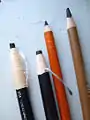 Til venstre 2 kulpenne i papirkapper til afrivning efterhånden som pennen bliver slidt.Til højre kulpenne i træ.