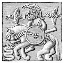 Del af hjelm, tynd, presset bronzeplade. Fundet i Vendel. Figuren forestiller muligvis Odin og hans to ravne Hugin og Munin.