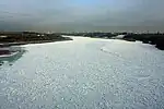 The surface of a wide river approaching a city is almost completely frozen.