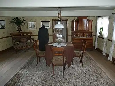 Stue med polerede møbler, tapet og petroleumslampe