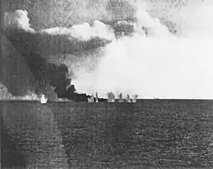 Eskorthangarskibe USS Gambier Bay i brand efter tidligere at være blevet ramt af granater bliver ramt af en salve fra en japansk krydser (svagt synlig i baggrunden) kort før den sank under Slaget ved Samar.