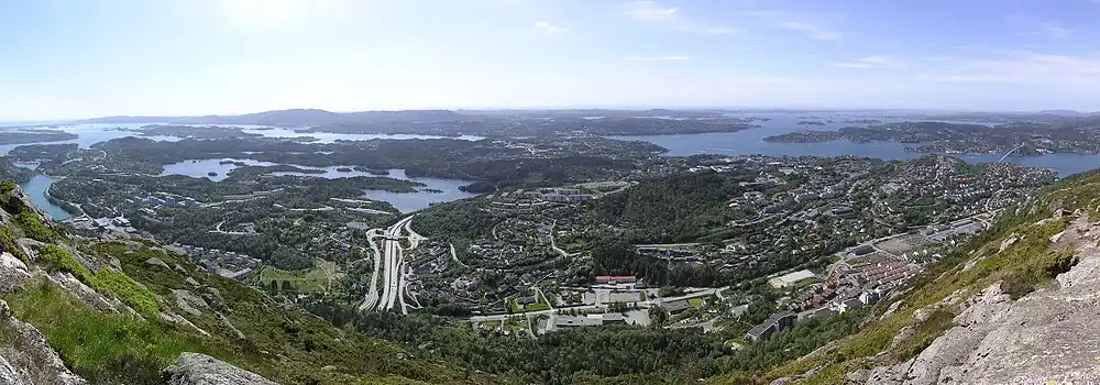 Udsigt mod vest fra Lyderhorn. Nedenunder ligger bydelen Loddefjord med busterminal og indkøbscenter. Helt til venstre Flesland lufthavn, og øverst i billedet ses øen Sotra. Til højre ligger Askøy og broen derud, "Askøybrua".