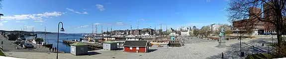 Rådhuspladsen og Rådhusbryggerne set vestover fra Akershus fæstnings side over Pipervika til Aker Brygge. Oslo Rådhus til højre. Havnepromenaden går langs vandet.