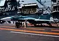 En Su-33 ombord på Admiral Kuznetsov i 1996. Personel fra U.S. Navys USS San Jacinto aflægger besøg på hangarskibet.