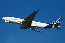 Et hvidt fly med blå markeringer letter mod en blå himmel.