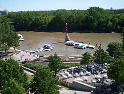 A muddy river floods a wooded urban area with boat docks and riverside seating.