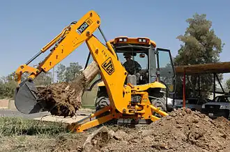 En JCB 3CX rendegraver. De vandrette støtteben er sænket så maskinen kan stå fast på jorden, så den ikke vælter mens den arbejder.