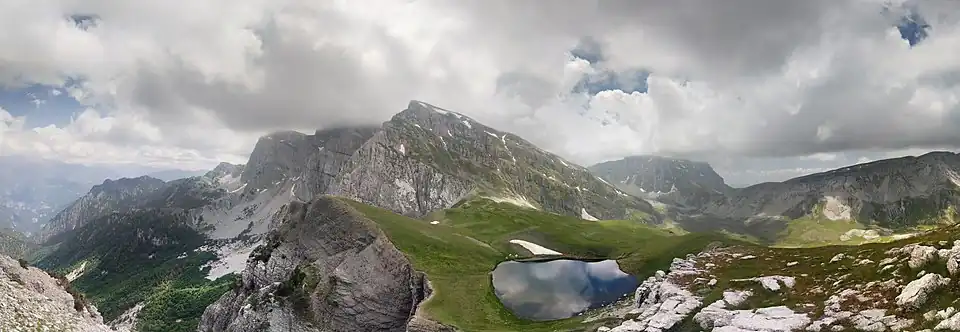Panoramaudsigt over Tímfi. Til venstre ses Gamíla-toppen i skyerne, i midten er Plóskos og under den en Drakolímni, til højre med toppen i skyer er Astráka og yderst til højre Lápatos. Ved grænsen mellem Astráka og Lapatos ligger bjerghytten D. Georgoulis.